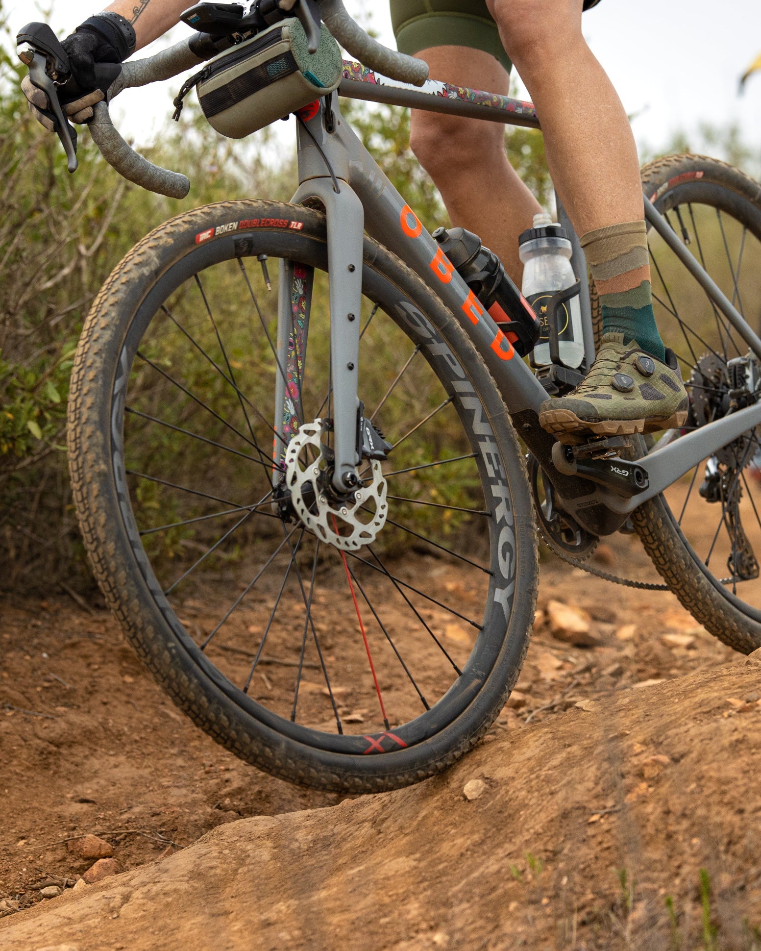 Two people riding bicycles on a dirt trail with a natural landscape.
